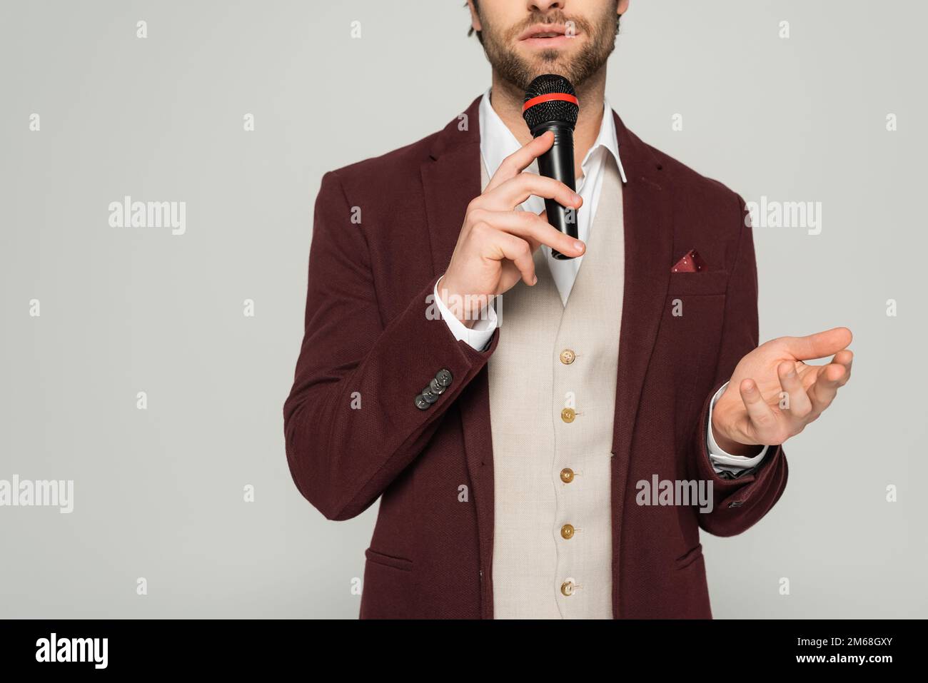 cropped view of bearded host of event in formal wear holding microphone ...