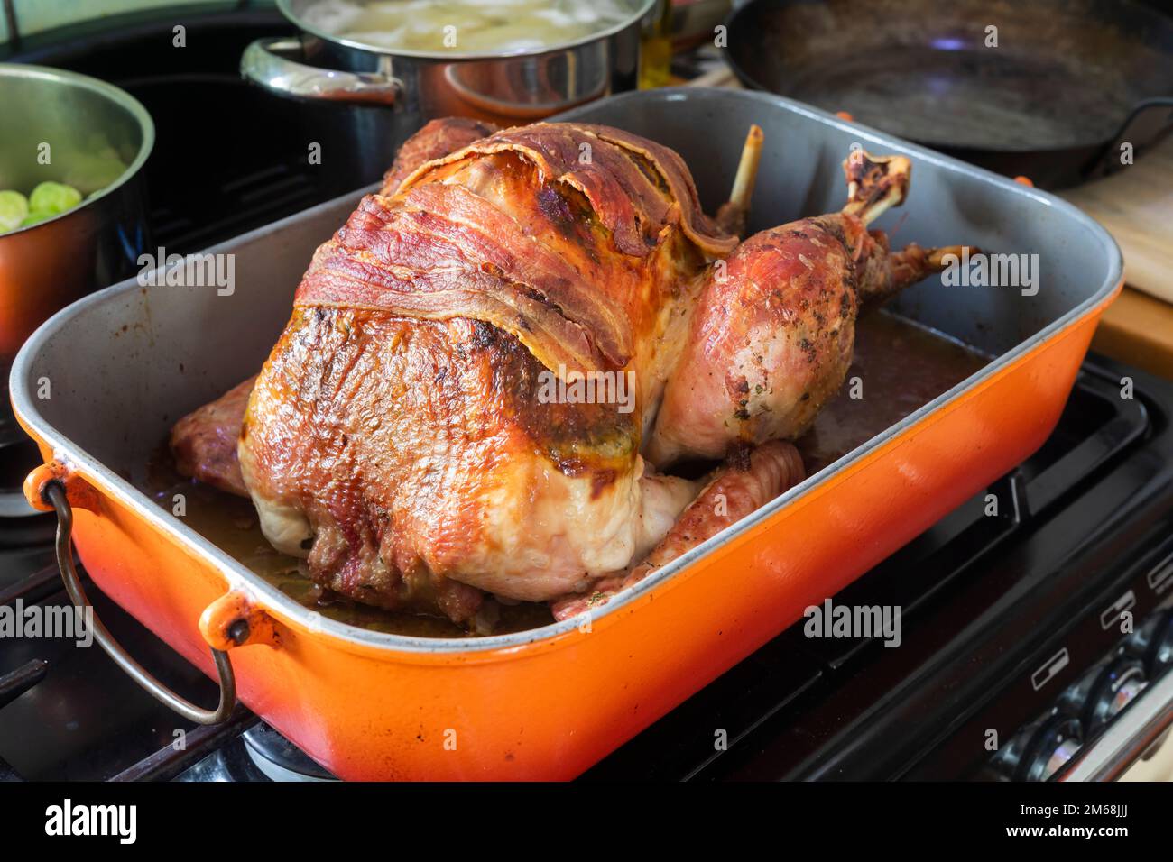 A cooked roast Bronze Turkey topped with streaky bacon rashers, resting on a cooker hob ready to be carved. Stock Photo