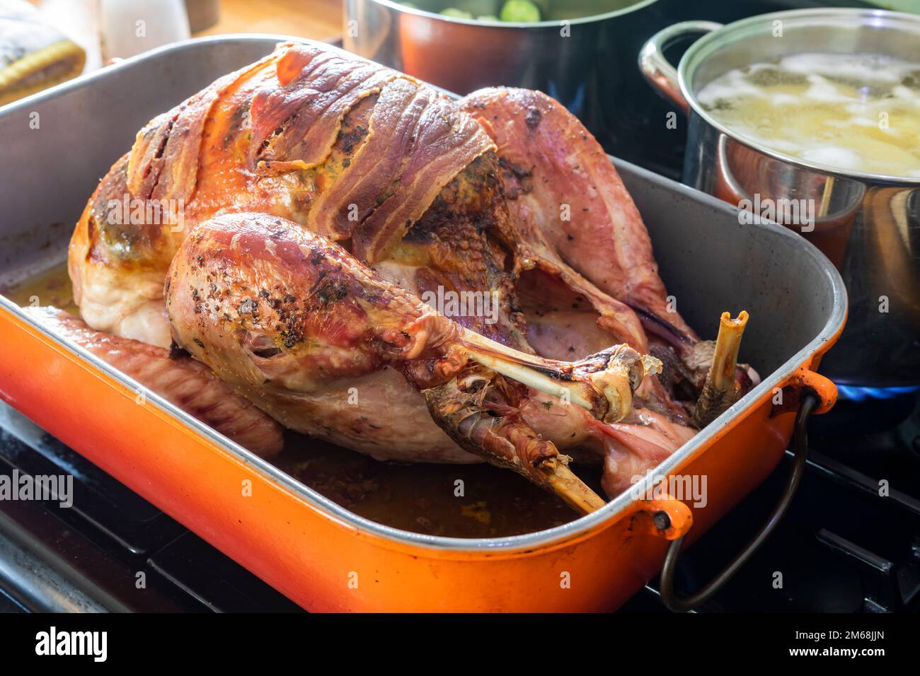 A cooked roast Bronze Turkey topped with streaky bacon rashers, resting on a cooker hob ready to be carved. Stock Photo