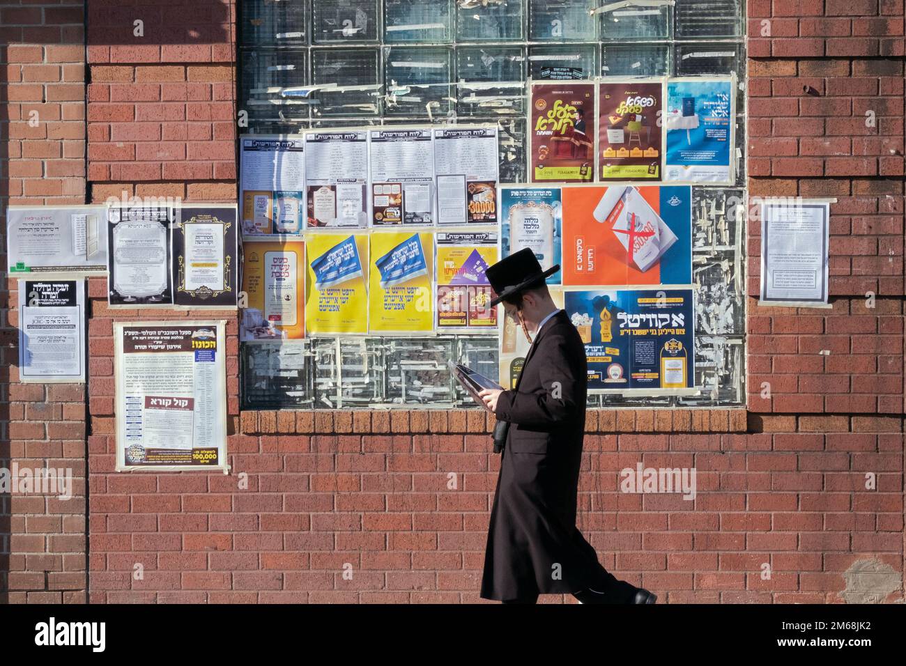 An orthodox jewish young man passes a community bulletin board on a  mild winter day in Brooklyn, New York. Stock Photo