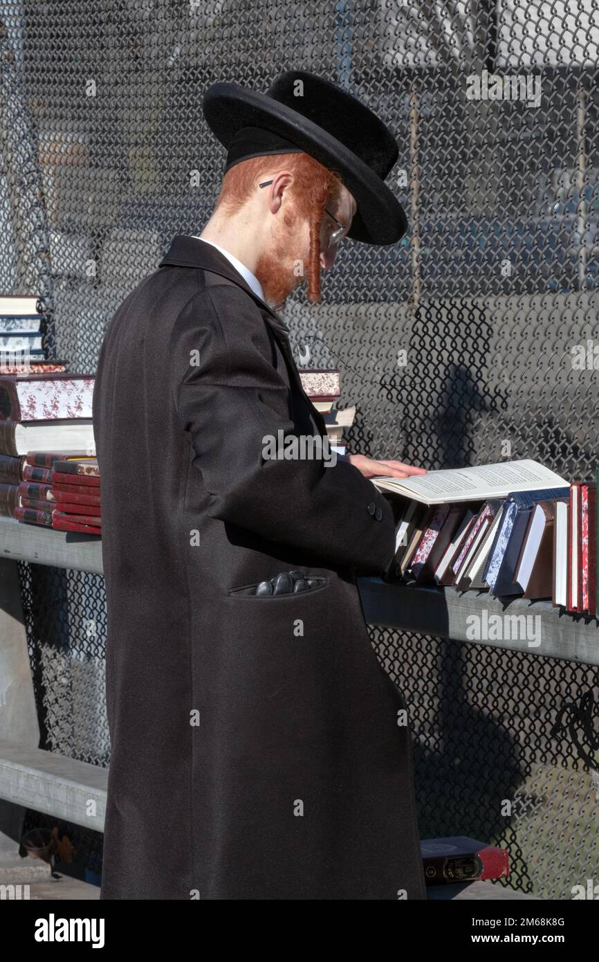 An ultra orthodox Jewish man with a red beard & red peyot shops for books on a mild winter Sunday. In Brooklyn, New York City. Stock Photo