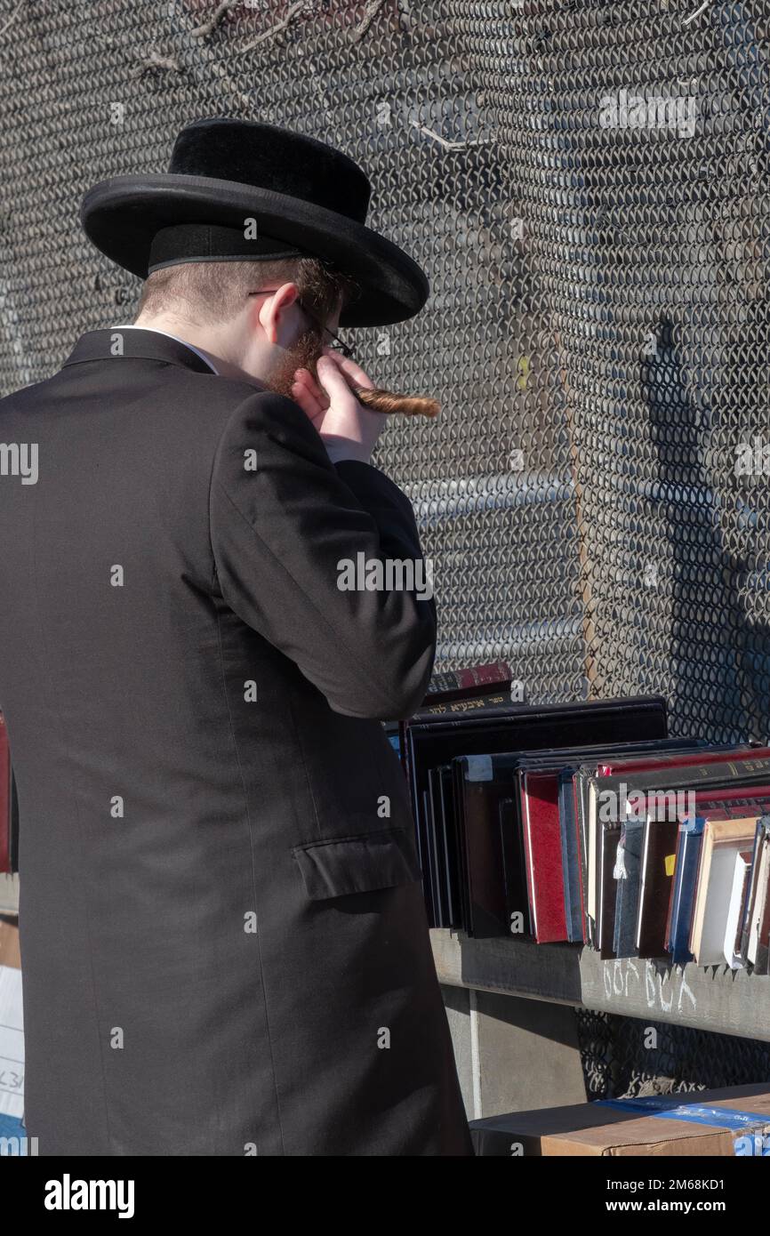 An orthodox jewish man with reddish brown hair twirls his long peyot while browsing books at an outdoor pop up store. In Brooklyn, New York. Stock Photo