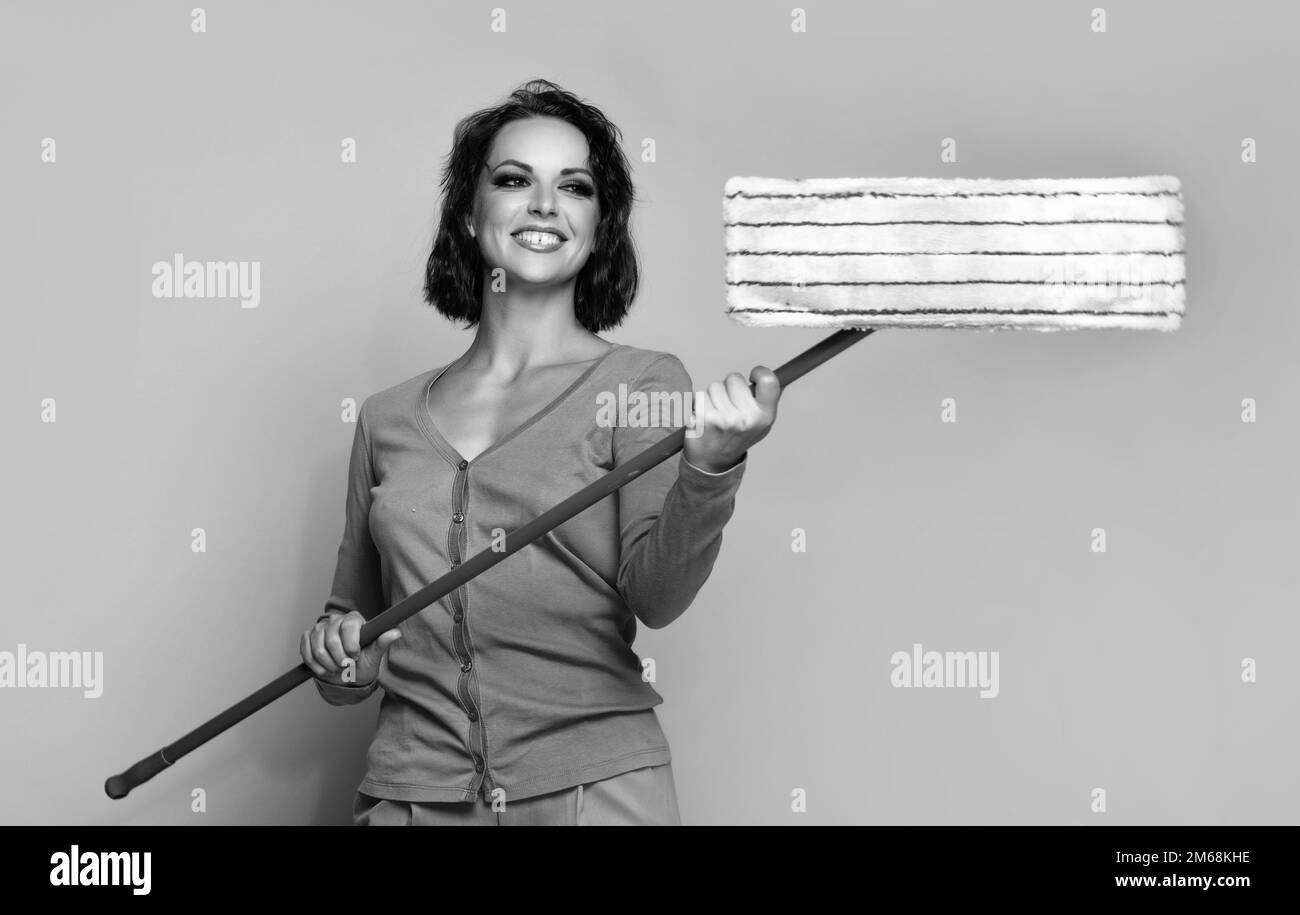 Happy young woman holding mop for doing chores beige background