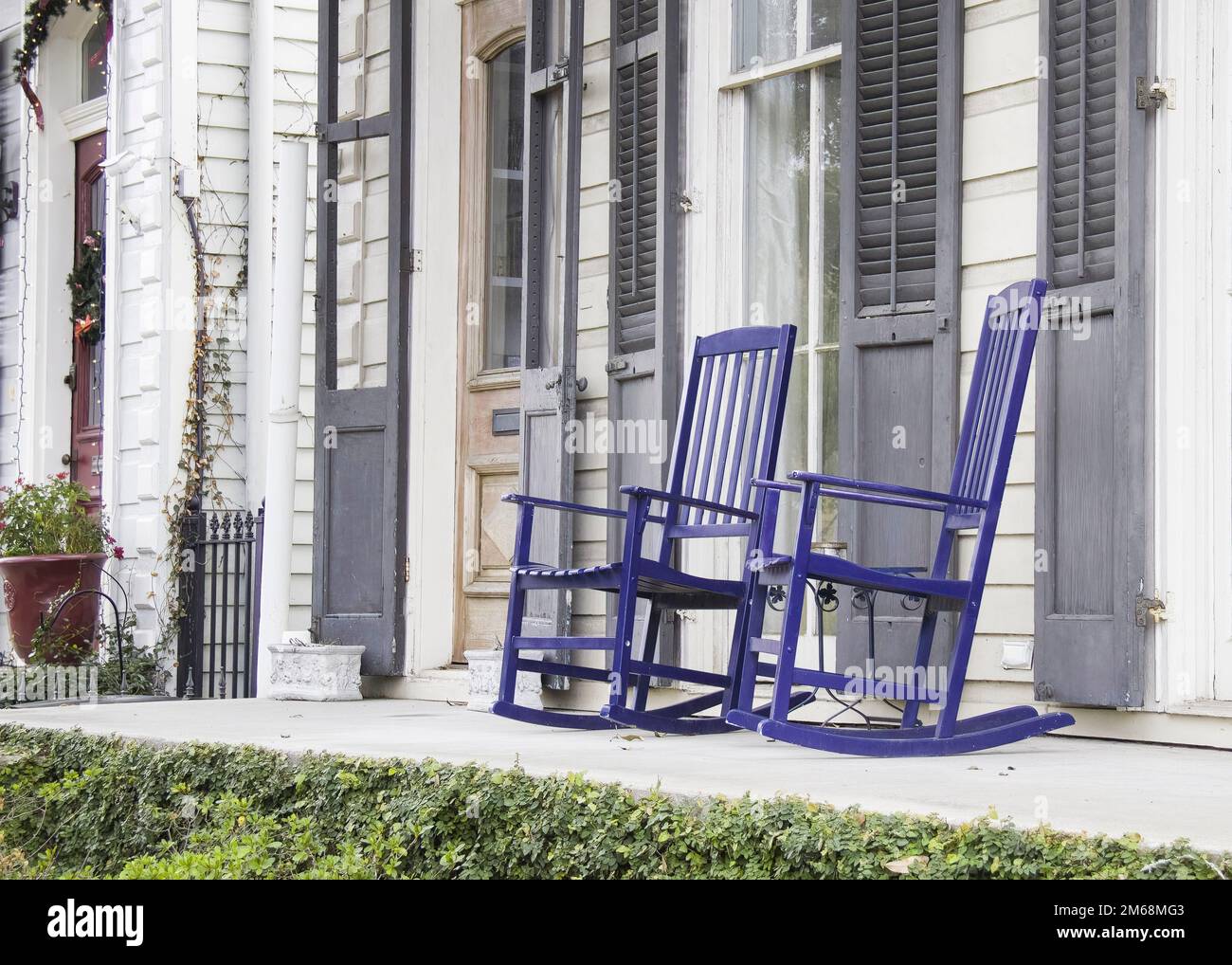 Two blue wooden rocking chairs on front porch of a southern USA colonial style home with grey shutters on windows and clapboard construct Stock Photo