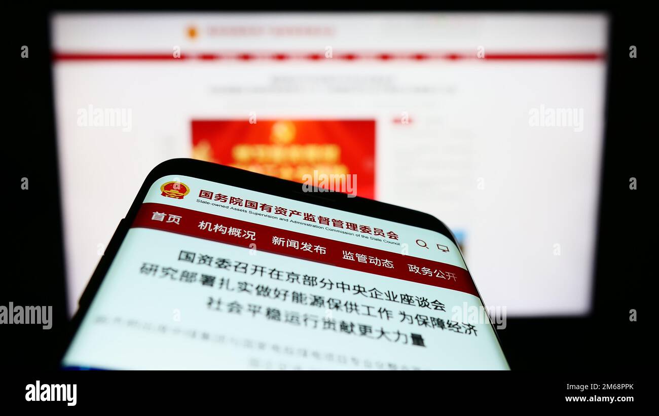 Mobile phone with web page and logo of Chinese state-owned special commission SASAC on screen. Focus on top-left of phone display. Stock Photo
