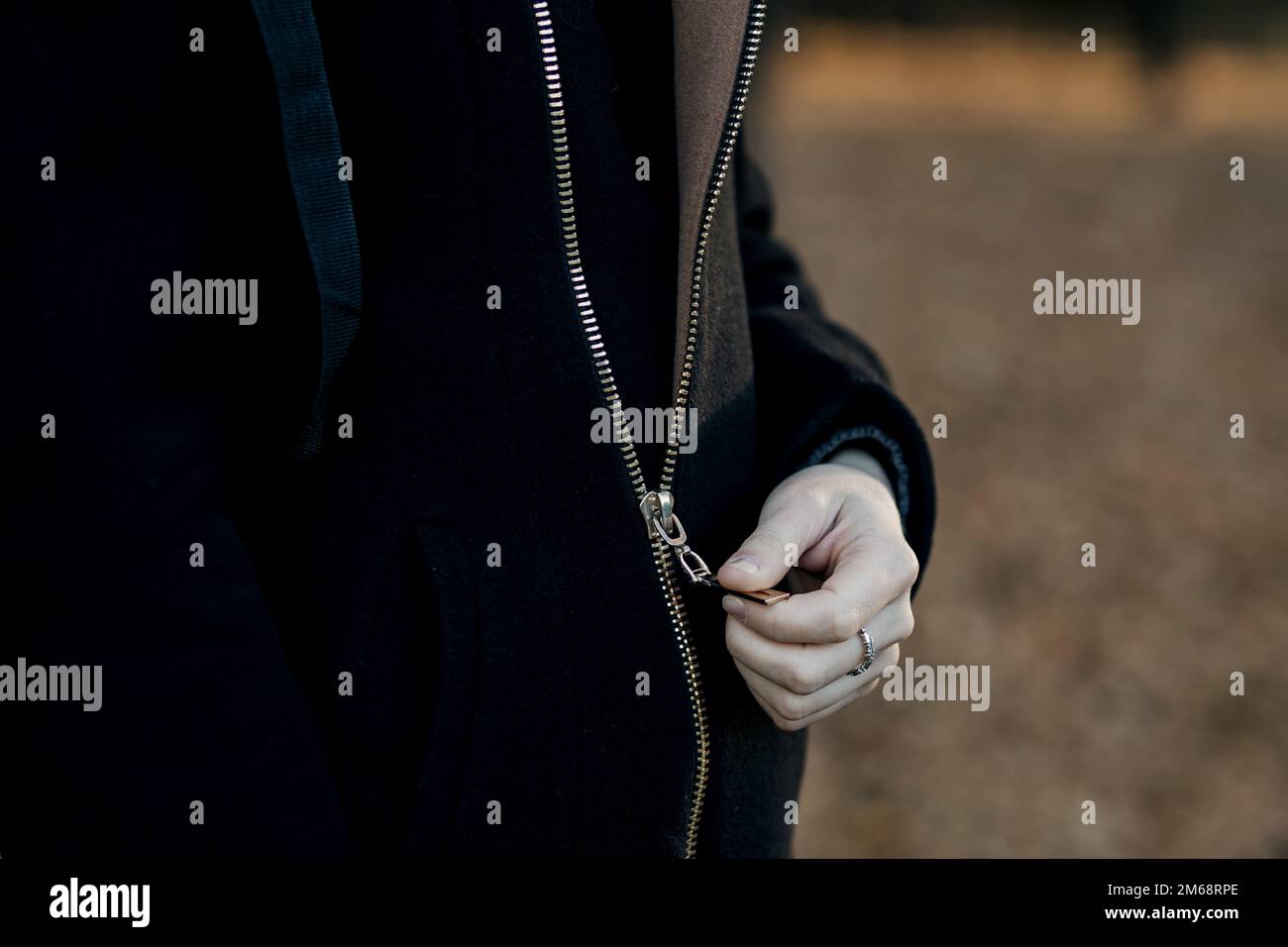 close-up of hands zipping up a jacket. a woman buttons up a black coat Stock Photo