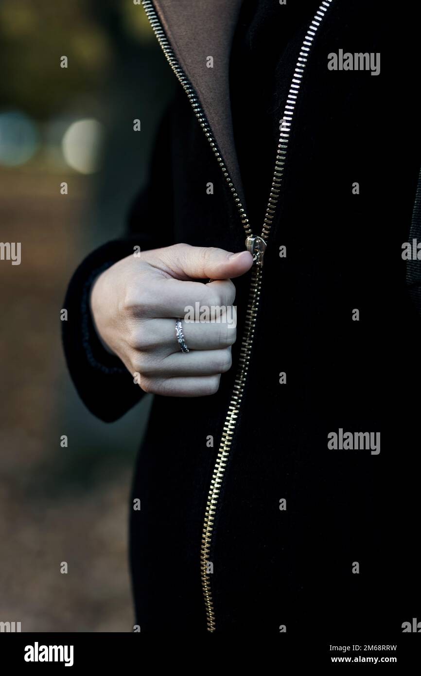 Close up of woman hands dressing closing zipper of black coat Stock Photo