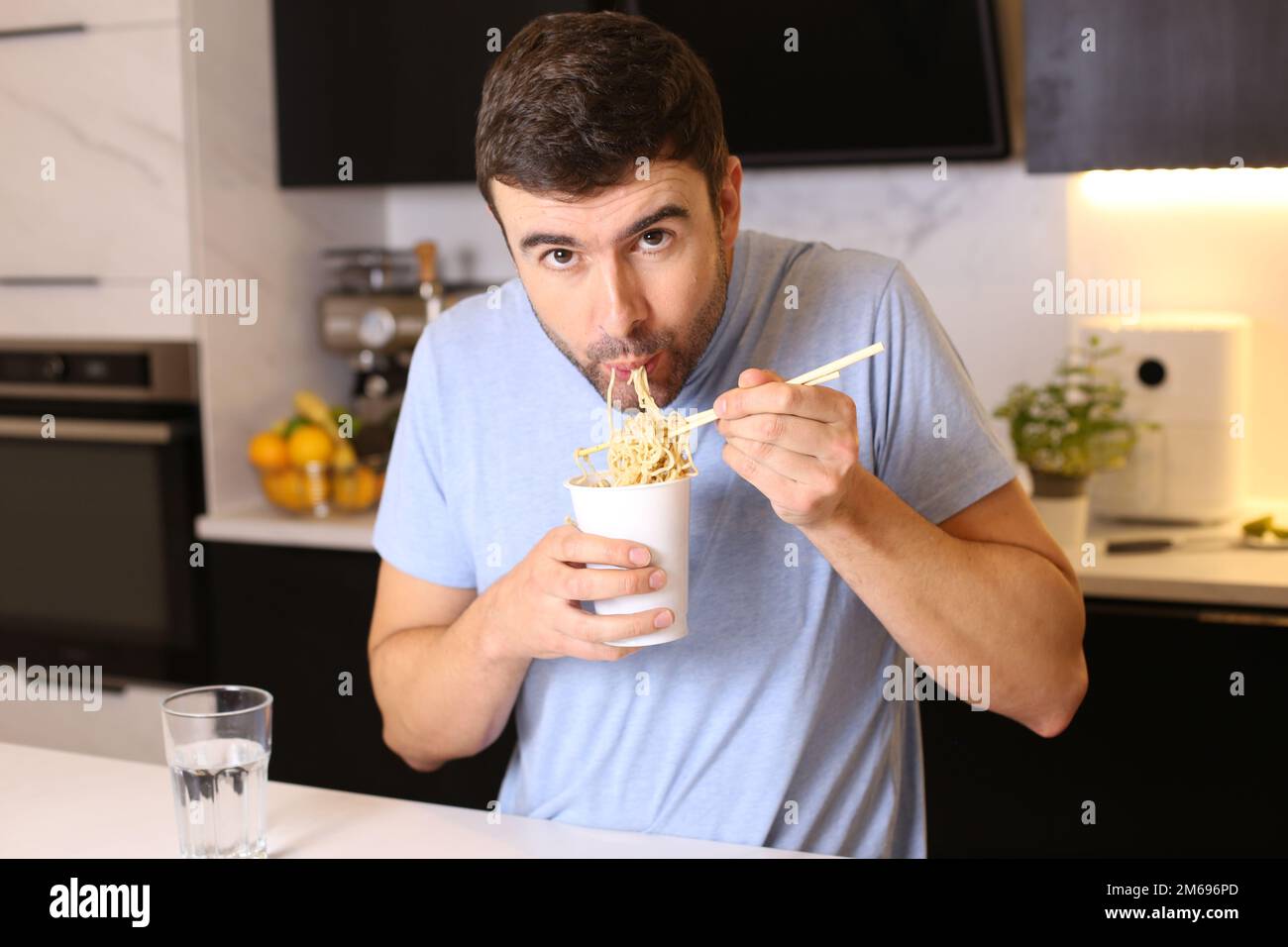 Cute guy eating instant noodles in the kitchen Stock Photo