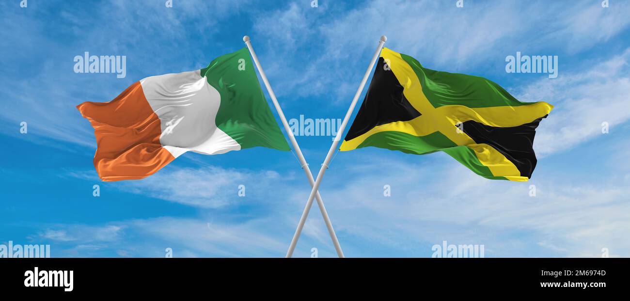 two crossed flags Jamaica and Ireland waving in wind at cloudy sky ...