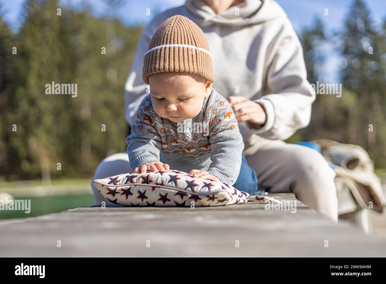 Happy family. Young mother playing with her baby boy infant oudoors on sunny autumn day. Portrait of mom and little son on wooden platform by lake. Positive human emotions, feelings, joy Stock Photo