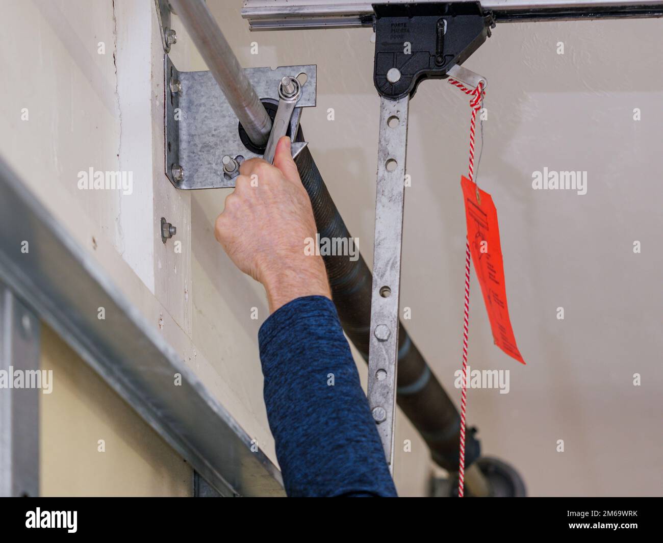 Man repairing electric garage door coiled tension spring. Installing and adjusting overhead garage door opener. Stock Photo