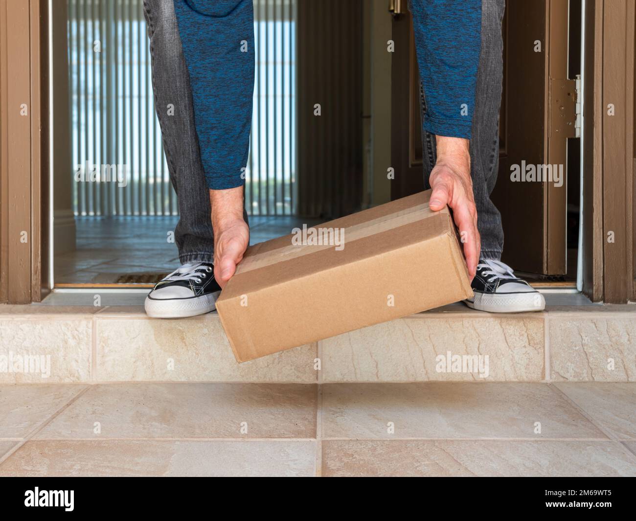 Man picking up a package box delivered to a residential doorstep. Online order package delivery to the front porch of home. Stock Photo