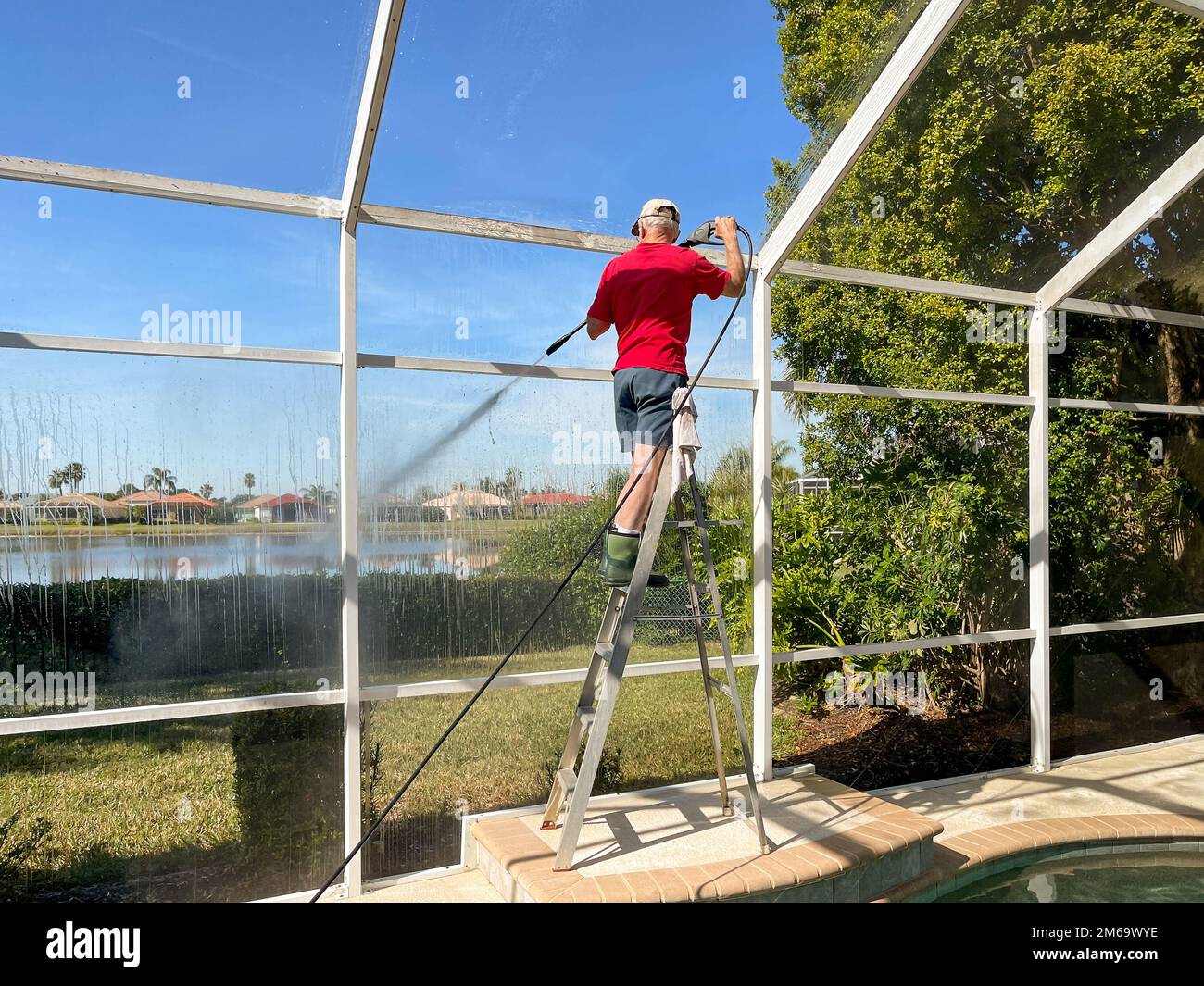 Handyman cleaning outdoor screen pool cage enclosure with power washer