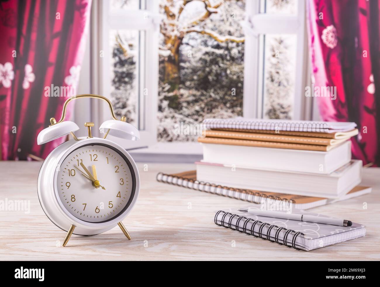 Winter semester, time management concept. Alarm clock with book, notenooks with open window in background Stock Photo