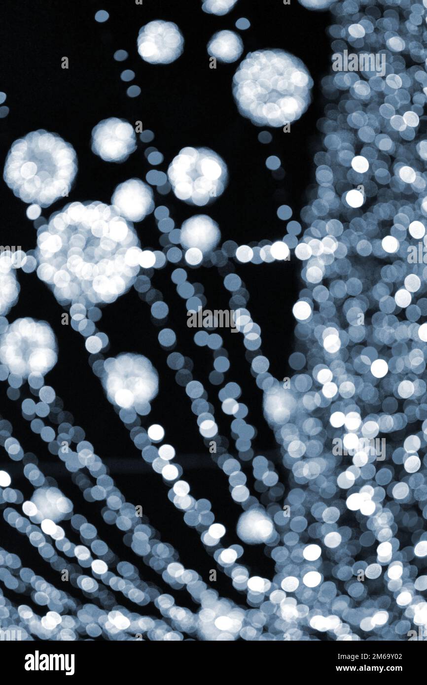 Blurred background. Beautiful luminous and flashing New Year Christmas decoration garlands and glowing balls for Christmas tree hanging outdoors night.Blurry blinking bokeh spots backdrop Blue color Stock Photo