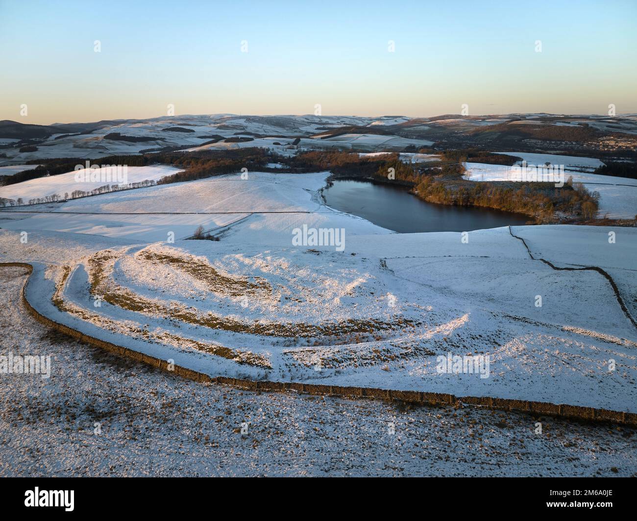 Aerial shot of Cauldhiels Hillfort with details picked up by snow and low winter sun and Cauldshiels Loch in the background. Stock Photo