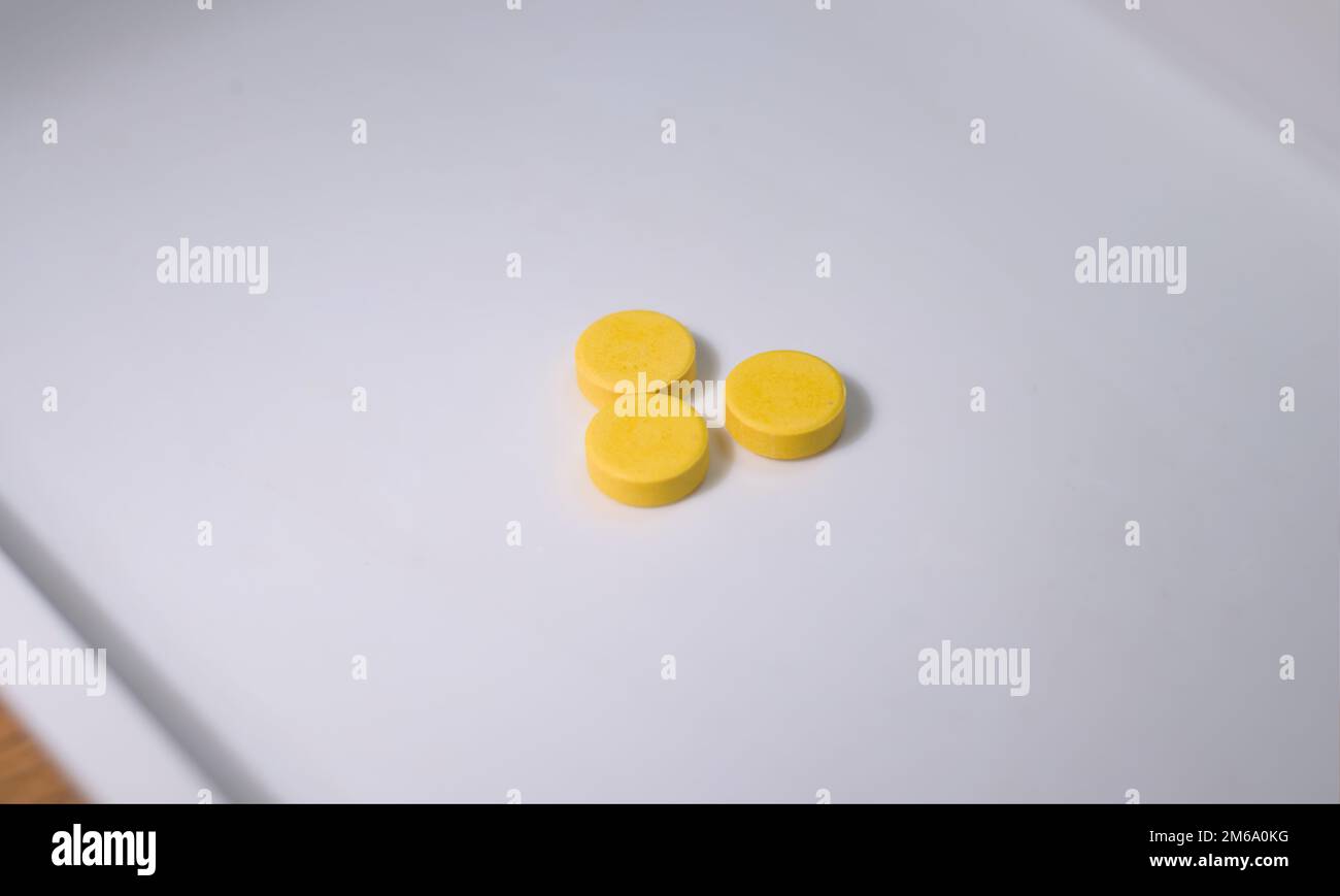 Three yellow pills or tablets medicine on a white surface. Close up. Stock Photo