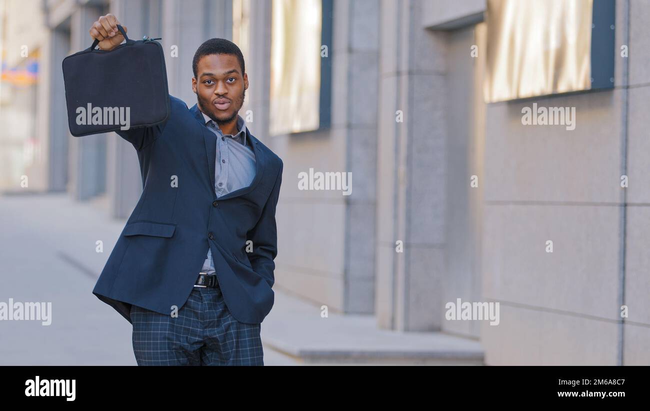 Confident proud male African American businessman excited man worker entrepreneur at city on street outdoors holding showing briefcase looking at Stock Photo