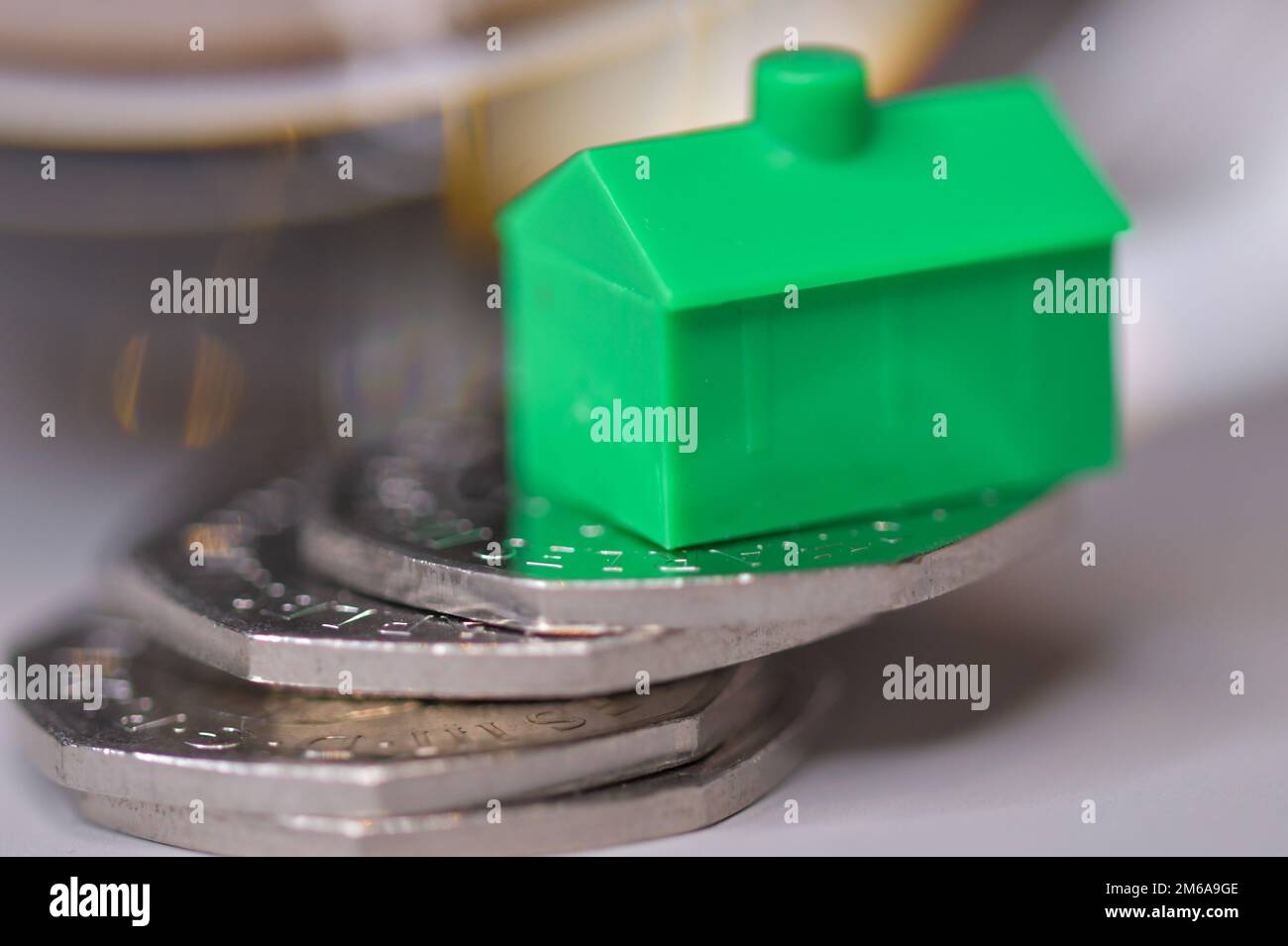 A green house balanced on a pile of 50 pence coins, housing market, stability, house prices, mortgage Stock Photo