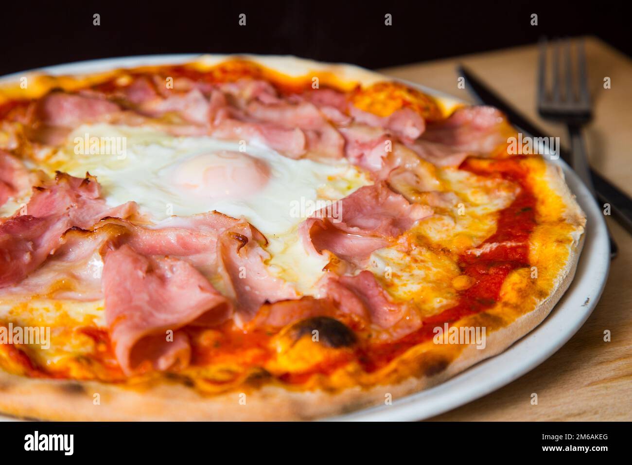 Prosciutto Pizza with egg in the middle. Neapolitan pizza with tomato sauce, cheese and