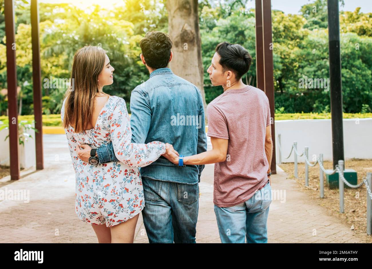 Unfaithful girl walking in the park with her boyfriend while holding another man hand. Love triangle concept. Woman holding hands with another man Stock Photo