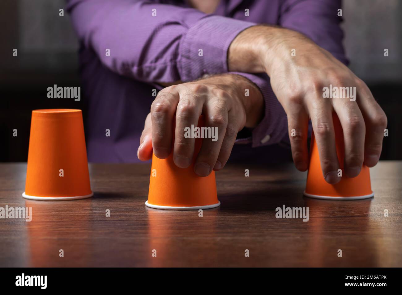 Man shows shell game of thimbles with coin, dark background. Concept deception, sleight hand Stock Photo