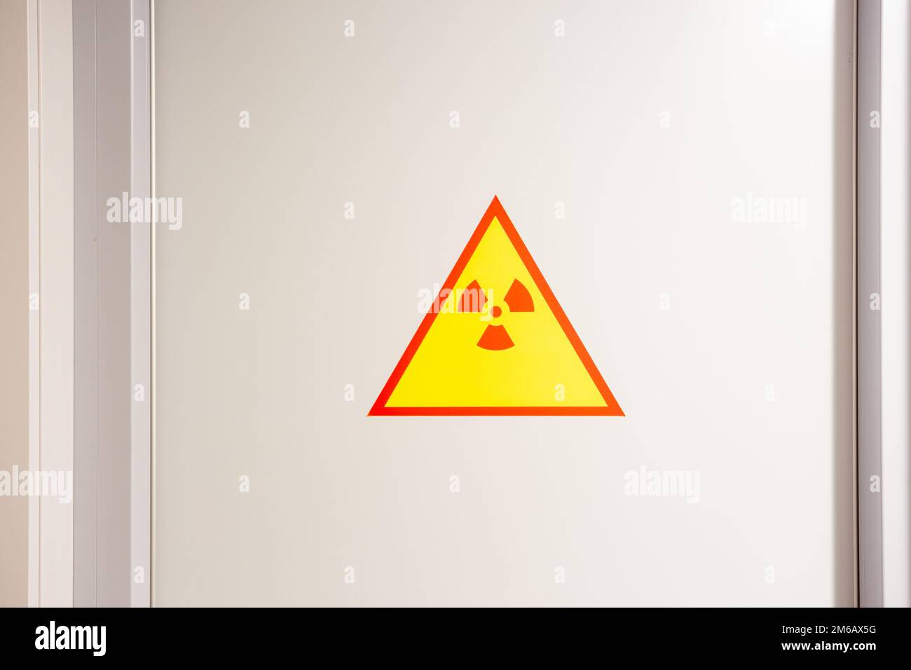 Red and yellow radiation precaution sign on the white steel wall. Caution symbol on lab door. Important information. Stock Photo