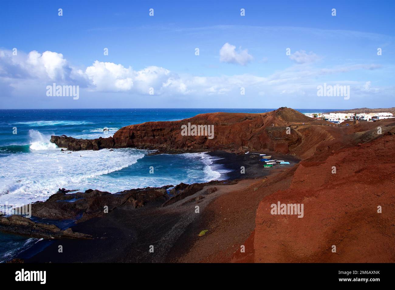 Charco de los Clicos, red lava rocks, surf, black lava beach, blue sky with white clouds, west coast, Lanzarote, Canary Islands, Spain Stock Photo