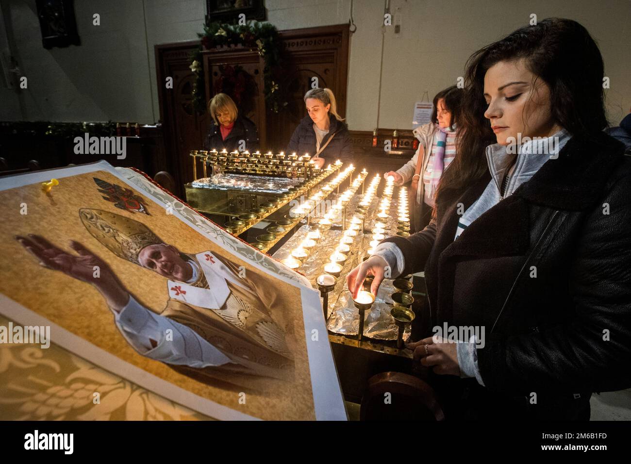 Lucy Knowles (right) lights a candle beside an image of Pope Emeritus Benedict XVI at St Mary’s Church in Belfast, Northern Ireland. Benedict, 95, died on Saturday after 10 years in an extraordinary papal retirement lived out in a monastery in the Vatican Gardens. Picture date: Tuesday January 3, 2023. Stock Photo