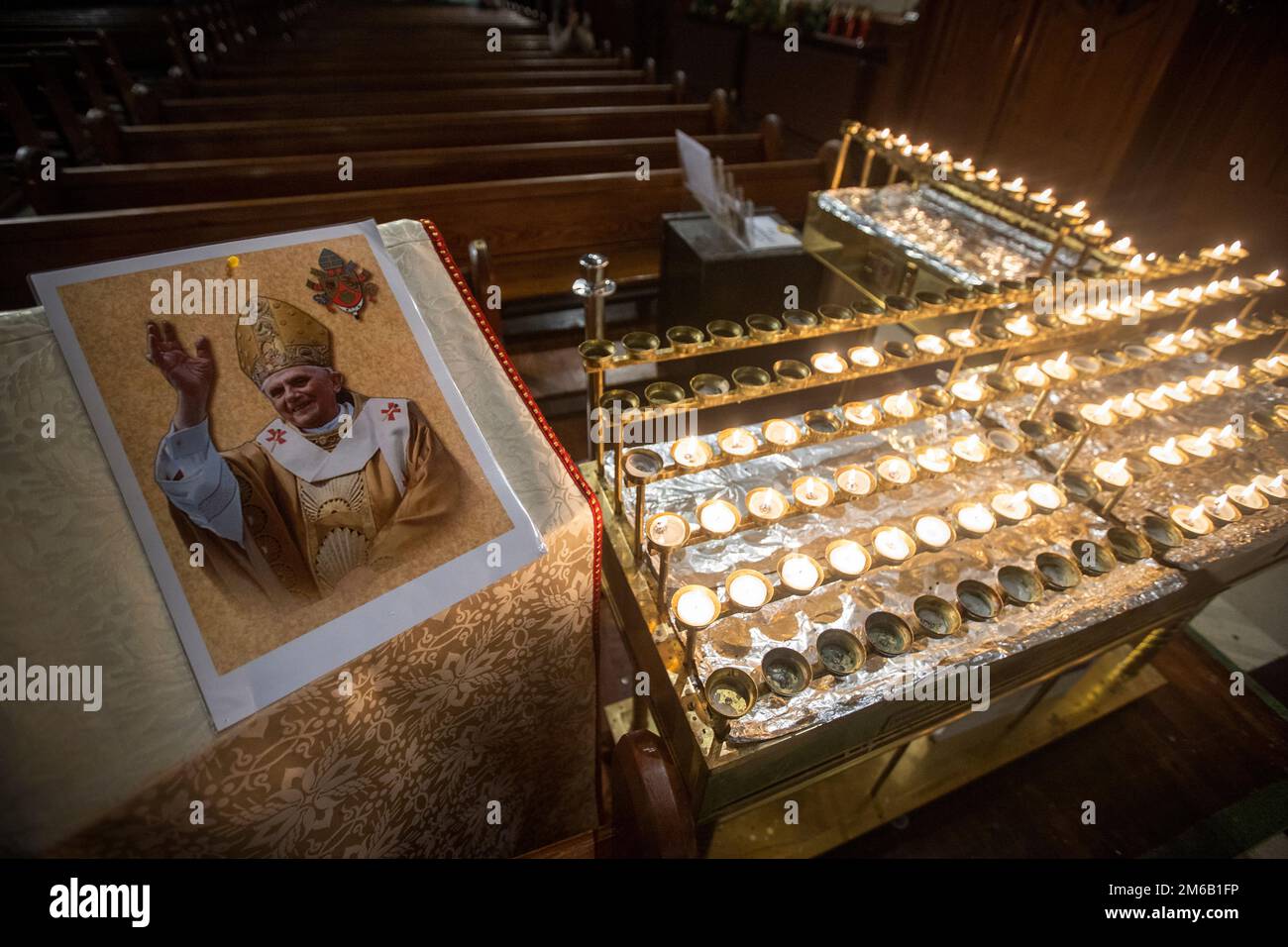 An image of Pope Emeritus Benedict XVI beside lit candles at St Mary’s Church in Belfast, Northern Ireland. Benedict, 95, died on Saturday after 10 years in an extraordinary papal retirement lived out in a monastery in the Vatican Gardens. Picture date: Tuesday January 3, 2023. Stock Photo