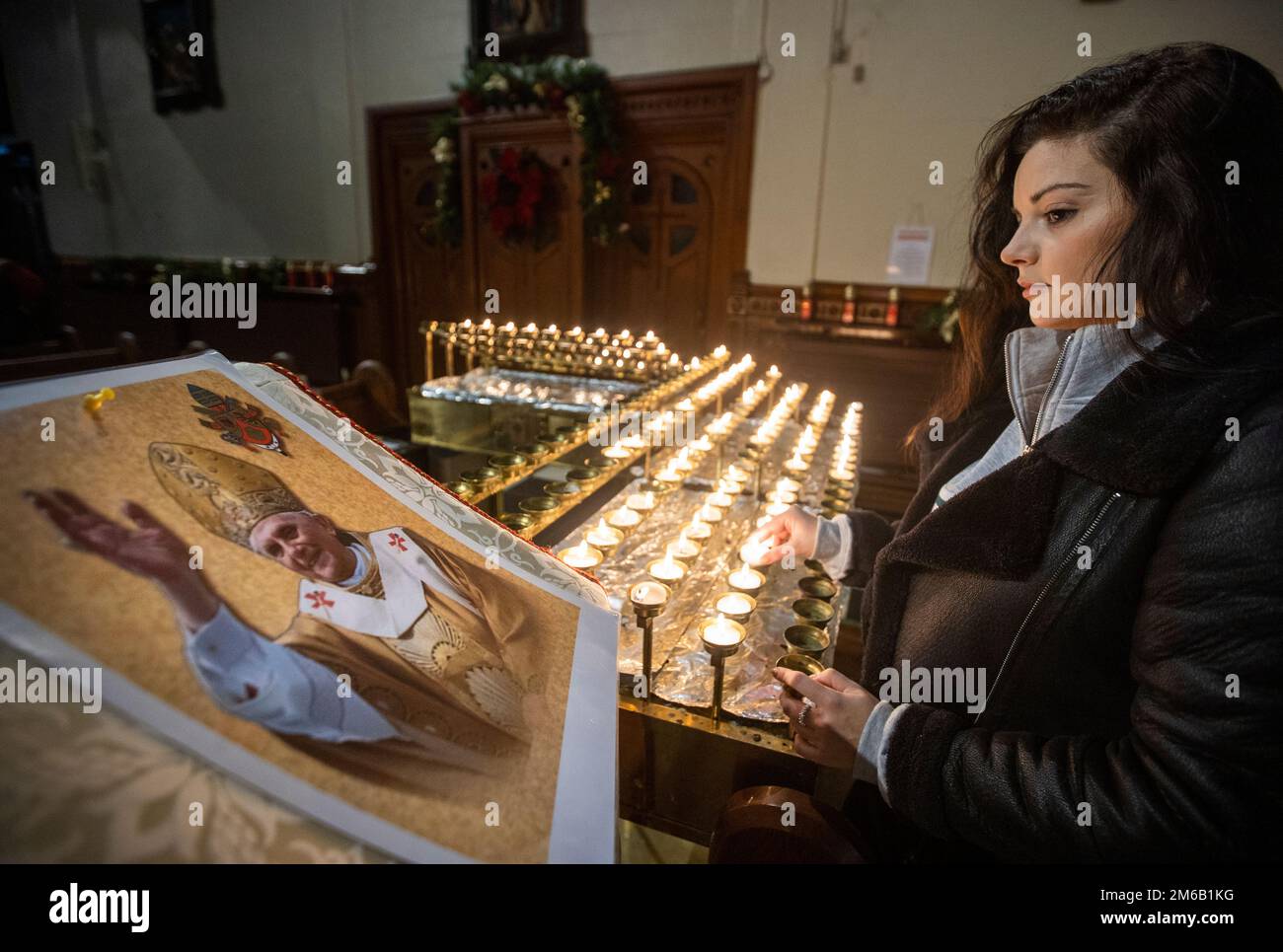 Lucy Knowles looks on at an image Pope Emeritus Benedict XVI as she lights a candle at St Mary’s Church in Belfast, Northern Ireland. Benedict, 95, died on Saturday after 10 years in an extraordinary papal retirement lived out in a monastery in the Vatican Gardens. Picture date: Tuesday January 3, 2023. Stock Photo