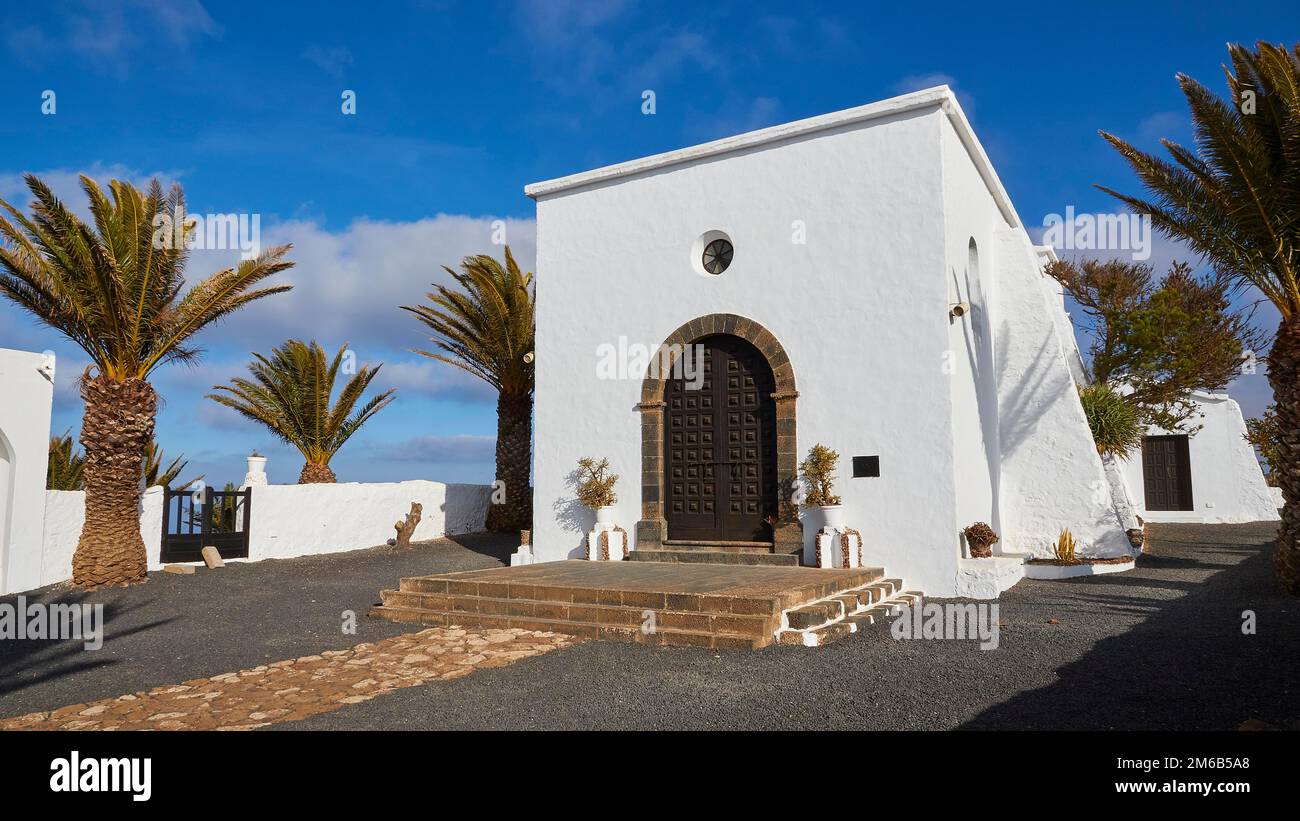 Ermita de las Nieves, hermitage, white building of the Ermita, stone framed, brown big wooden door, white stone wall, palm trees, blue sky with white Stock Photo
