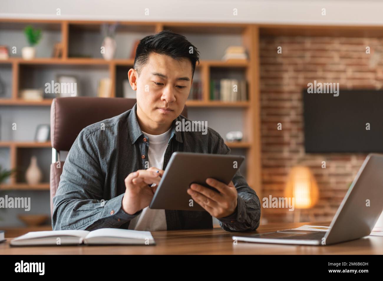 Serious concentrated middle aged asian guy typing on tablet, planning startup, analyze data at workplace Stock Photo