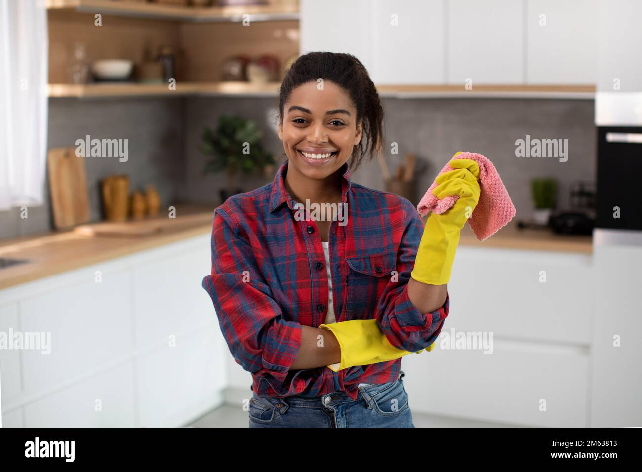Cheerful pretty millennial african american housewife in rubber gloves with rag enjoy household chores Stock Photo