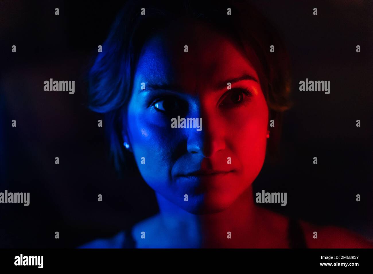The face of a young woman in blue and red neon light on a dark background. Stock Photo