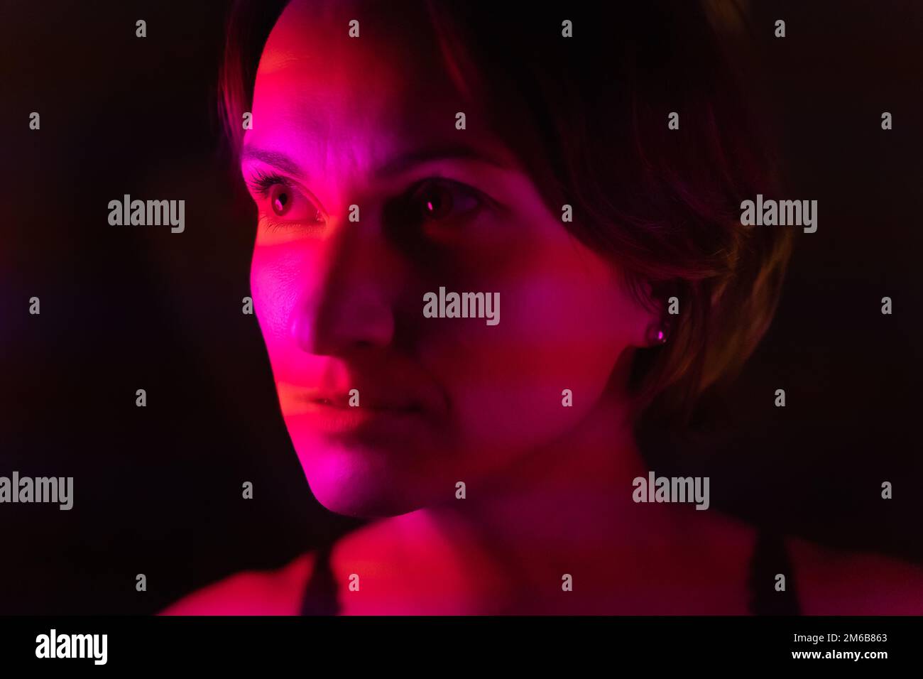 Close-up portrait of a young woman illuminated by stripes of pink and red. Stock Photo