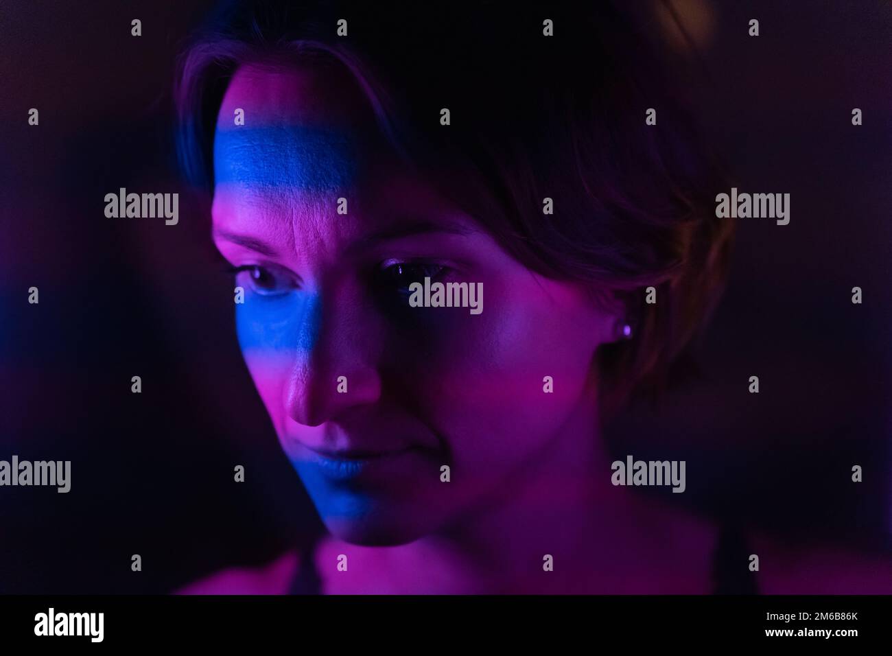 Stripes of blue and purple or purple neon light up the face of a young dark-haired woman. Stock Photo