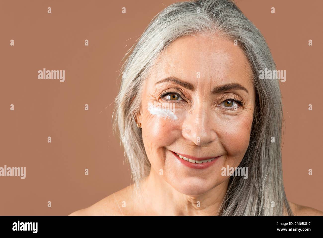 Happy old caucasian lady with natural beauty and cream on her face enjoy professional cosmetics Stock Photo