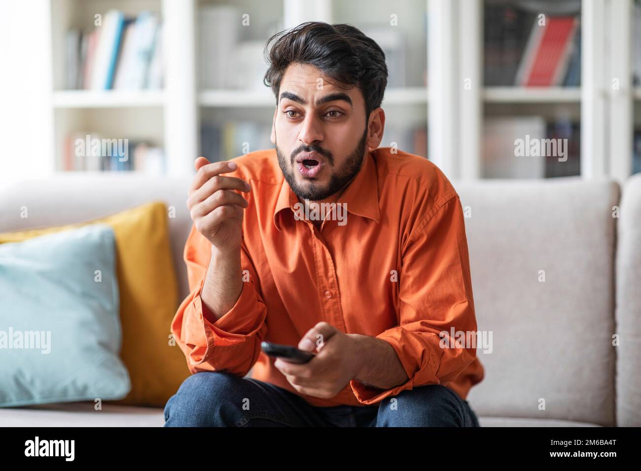 Shocked middle eastern guy sitting at home, switching tv Stock Photo