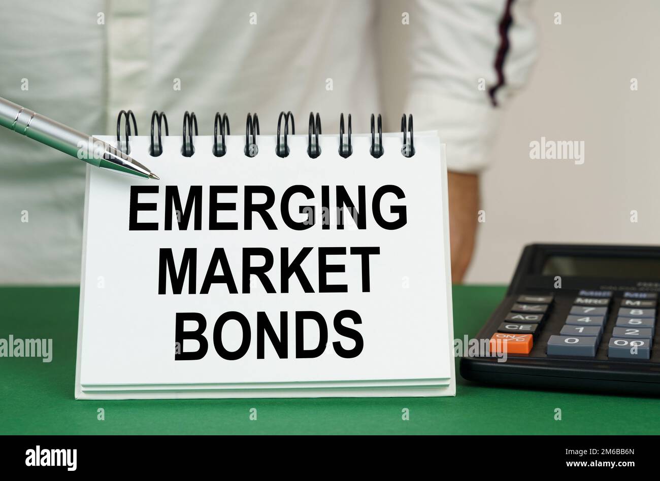 Business concept. On a green surface is a calculator, a man points with a pen to a notebook with the inscription - emerging market bonds Stock Photo