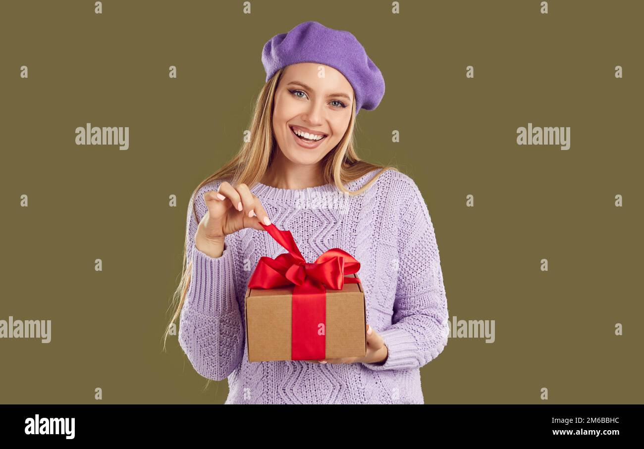 Beautiful and cute woman with joyful facial expression is untying ribbon on gift box. Stock Photo