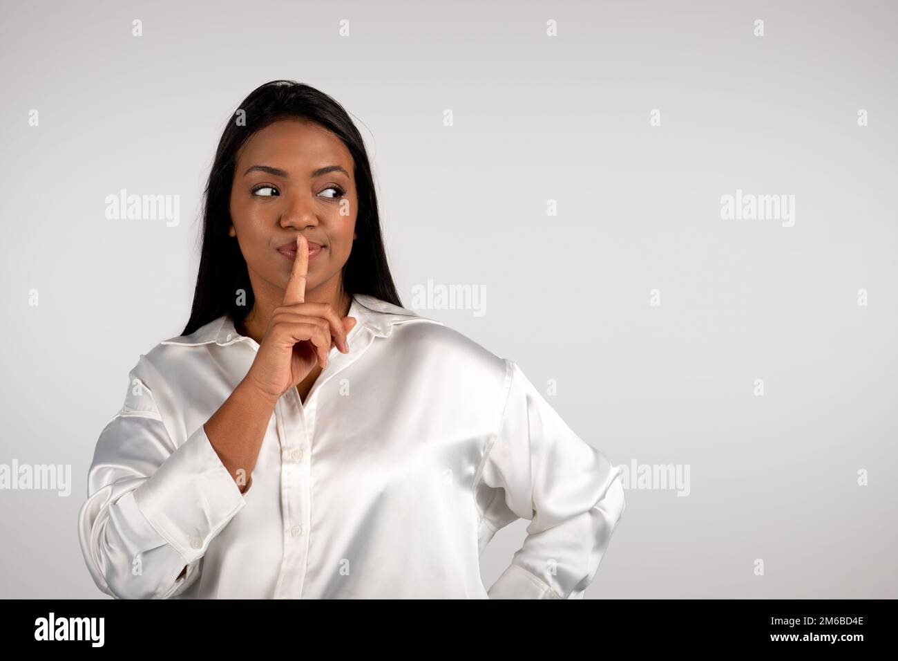 Pensive young african american business woman presses finger to lips, making shhh sign, looks at empty space Stock Photo