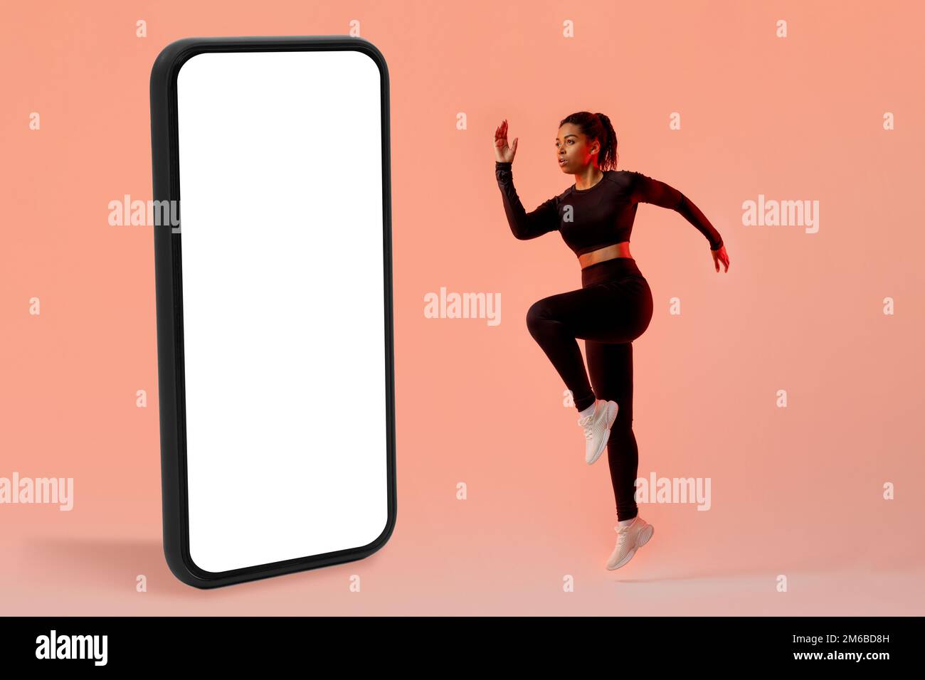 Workout application concept. Slim lady exercising near big cellphone, jumping in studio over neon background, mockup Stock Photo