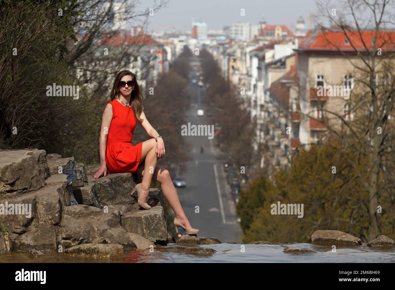 Beautiful blonde woman with orange dress sitting on a rock in a park ...