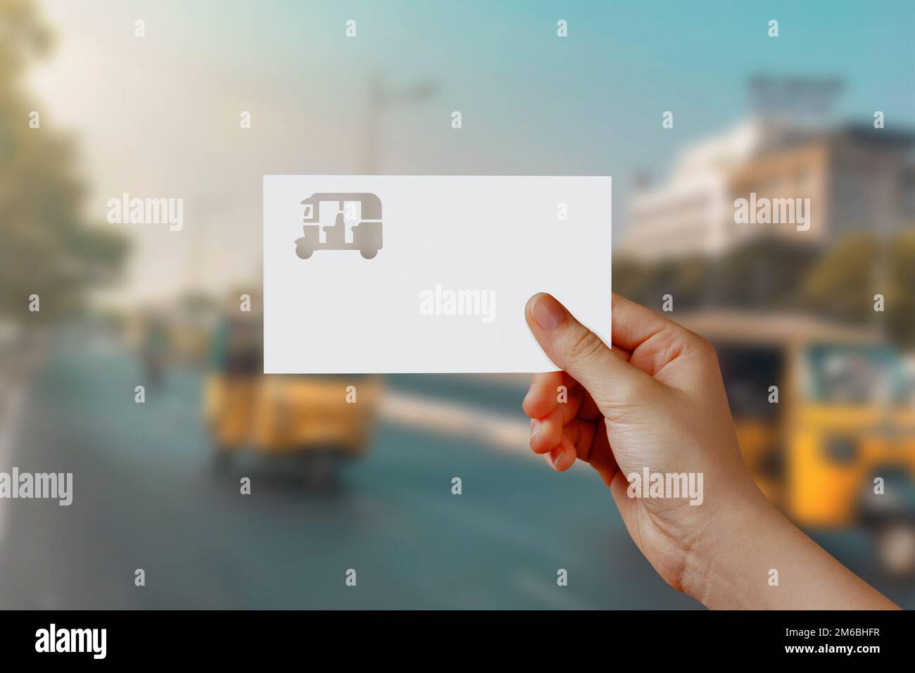 Man's hand holding Auto Rickshaw symbol paper on road. Concept of journey, travel, dream, freedom. Hand is holding paper Auto Rickshaw against road wi Stock Photo