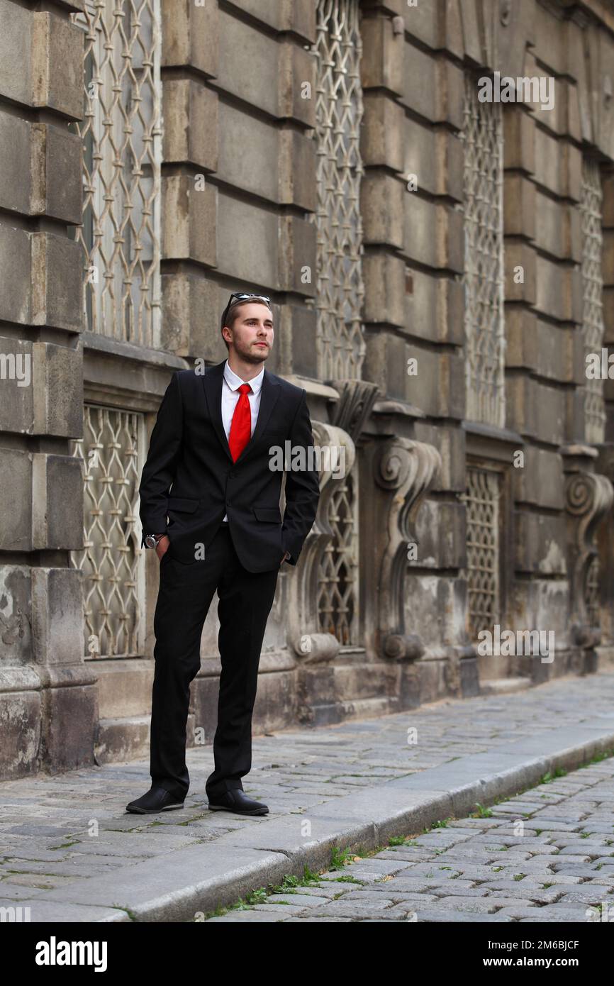 Young handsome man in black suit with red tie on the street Stock Photo