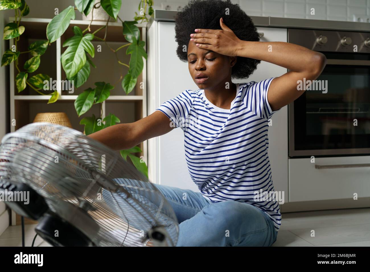 Exhausted young African woman having hot flashes sitting in front of
