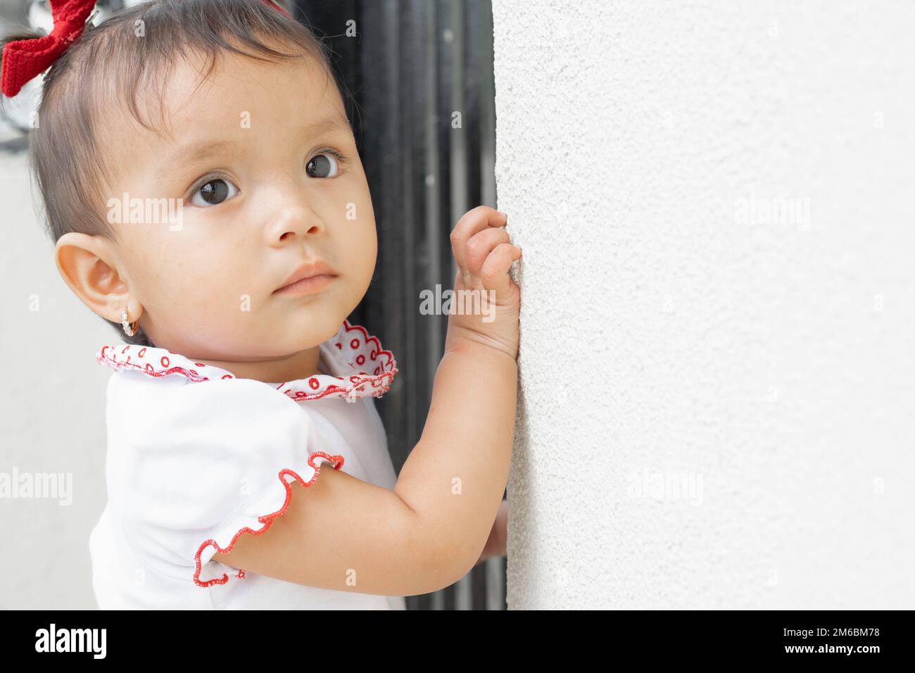 beautiful baby brunette latina, with her hand placed on the wall to hold herself up and not fall, while looking serious and curiously Stock Photo