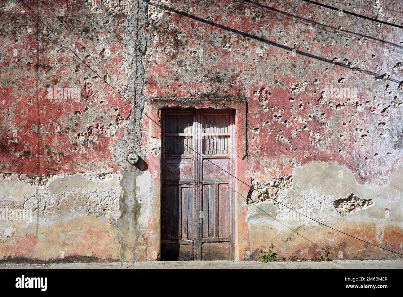 Old wooden door and crumbling pink stone wall in Valladolid, Yucatan, Mexico Stock Photo