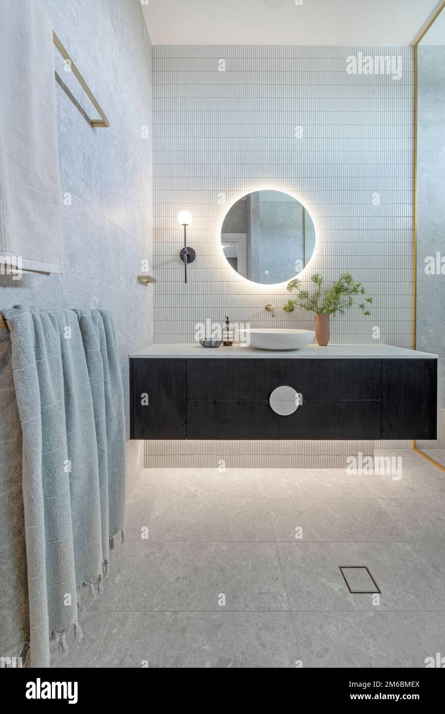 A new modern styled bathroom showing showing and a floating vanity with a back lit mirror and wall to floor tiling Stock Photo